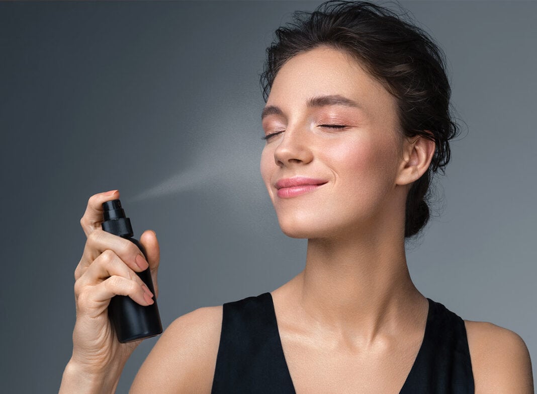 Junge Frau sprüht fixing spray über Ihr Make Up